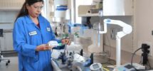 A female scientist in a blue lab coat working with aerosol measurement equipment.