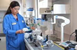 A female scientist in a blue lab coat working with aerosol measurement equipment.