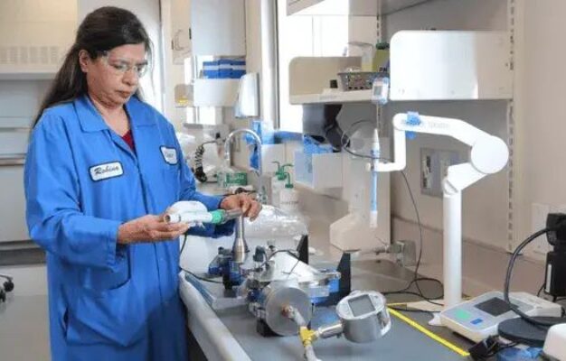 A female scientist in a blue lab coat working with aerosol measurement equipment.