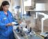 A female scientist in a blue lab coat working with aerosol measurement equipment.