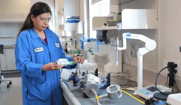 A female scientist in a blue lab coat working with aerosol measurement equipment.